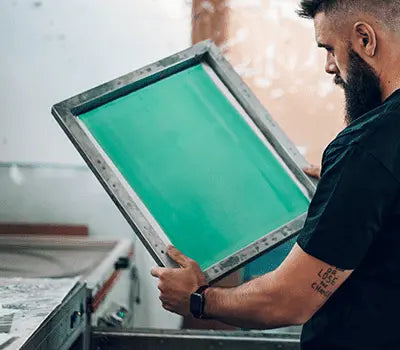 Person holding a green screen printing frame in a studio, showcasing essential screen printing supplies.