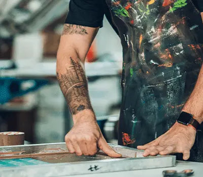 Person preparing screen printing supplies with hands on squeegee in a creative workspace.