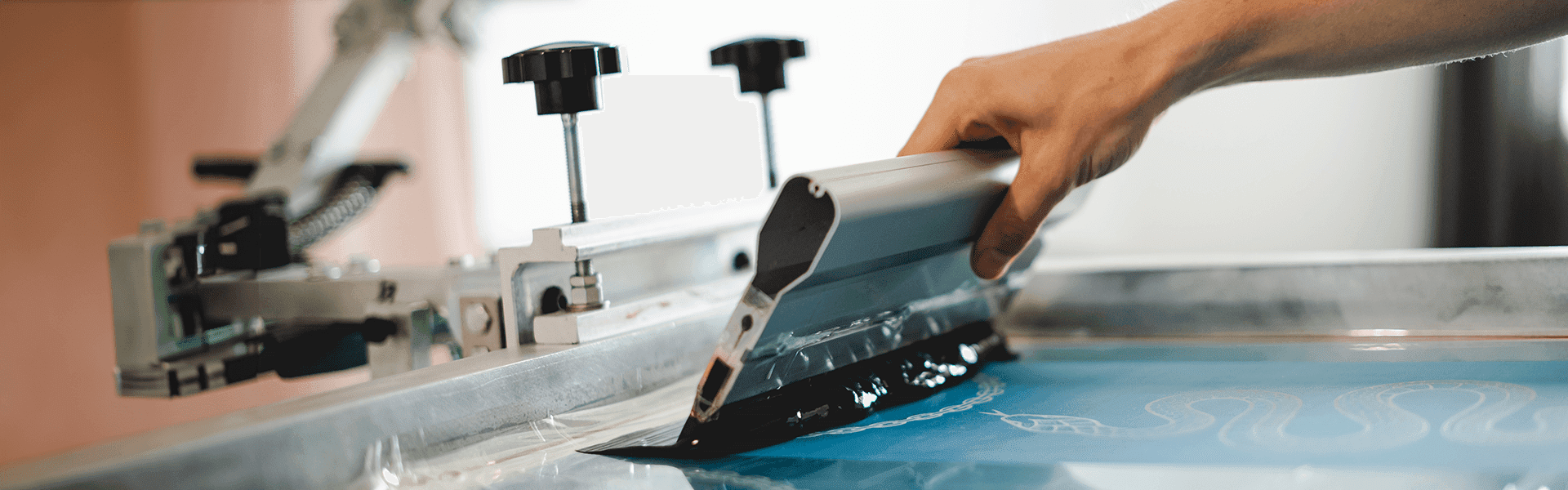 Person using a squeegee on a screen printing press, showcasing essential screen printing kits for DIY projects.