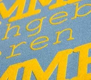 Close-up of blue fabric with yellow screen printed text, showcasing high-quality print for apparel decoration.